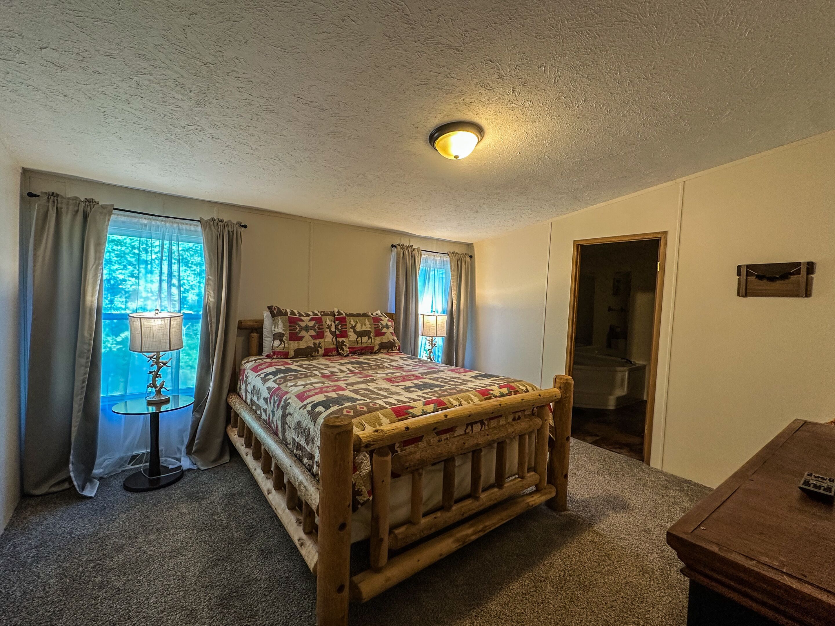 Une chambre à coucher avec un lit en bois, une table de chevet, une lampe et une fenêtre avec des rideaux.