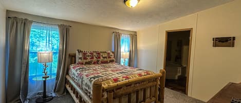 A bedroom with a wooden bed, a nightstand, a lamp, and a window with curtains.