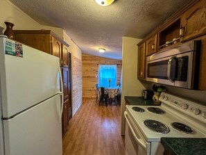 A compact kitchen with wooden cabinets, a refrigerator, a microwave, and a stove. - Spacious Eagle's Landing Cabin near Hocking Hills (Nelsonville)
