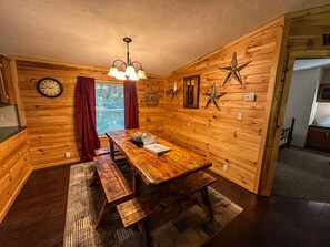 A wooden interior with a wooden table, benches, a clock, and star decorations.