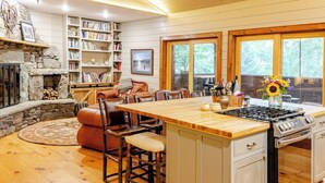 A cozy kitchen with a central island, wooden cabinets, and a stone fireplace. - Secluded waterfront home, minutes from Lake Placid and Saranac Lake (Saranac Lake)