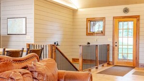 A spacious living room with a large brown leather sofa, wooden flooring, a staircase with a railing, and a wooden door with a window. - Secluded waterfront home, minutes from Lake Placid and Saranac Lake (Saranac Lake)