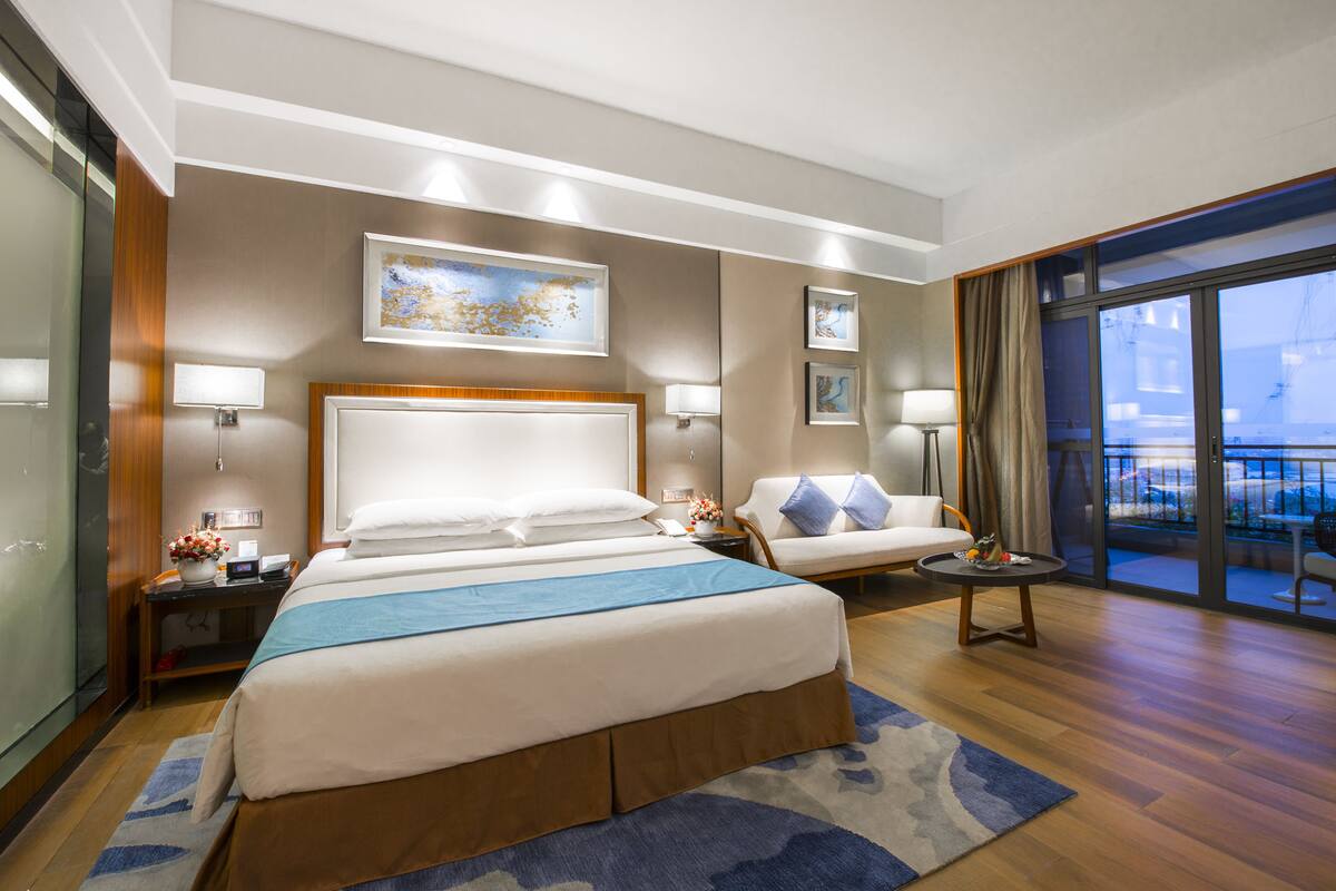 Ein Hotelzimmer mit einem großen Bett, einer Sitzecke, einem kleinen Tisch und einem Balkon mit Blick.