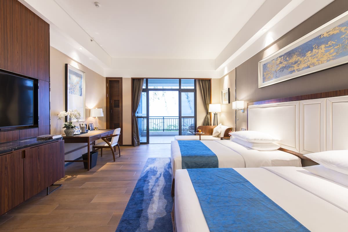 Ein Hotelzimmer mit zwei Betten, einem Schreibtisch, einem Fernseher und einem Balkon mit Blick.
