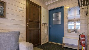 A room with a wooden door, a blue door, a white shelf, a fire extinguisher, and a grey couch. - Hil-lak-ka ii as 7 by Interhome (Äkäslompolo)