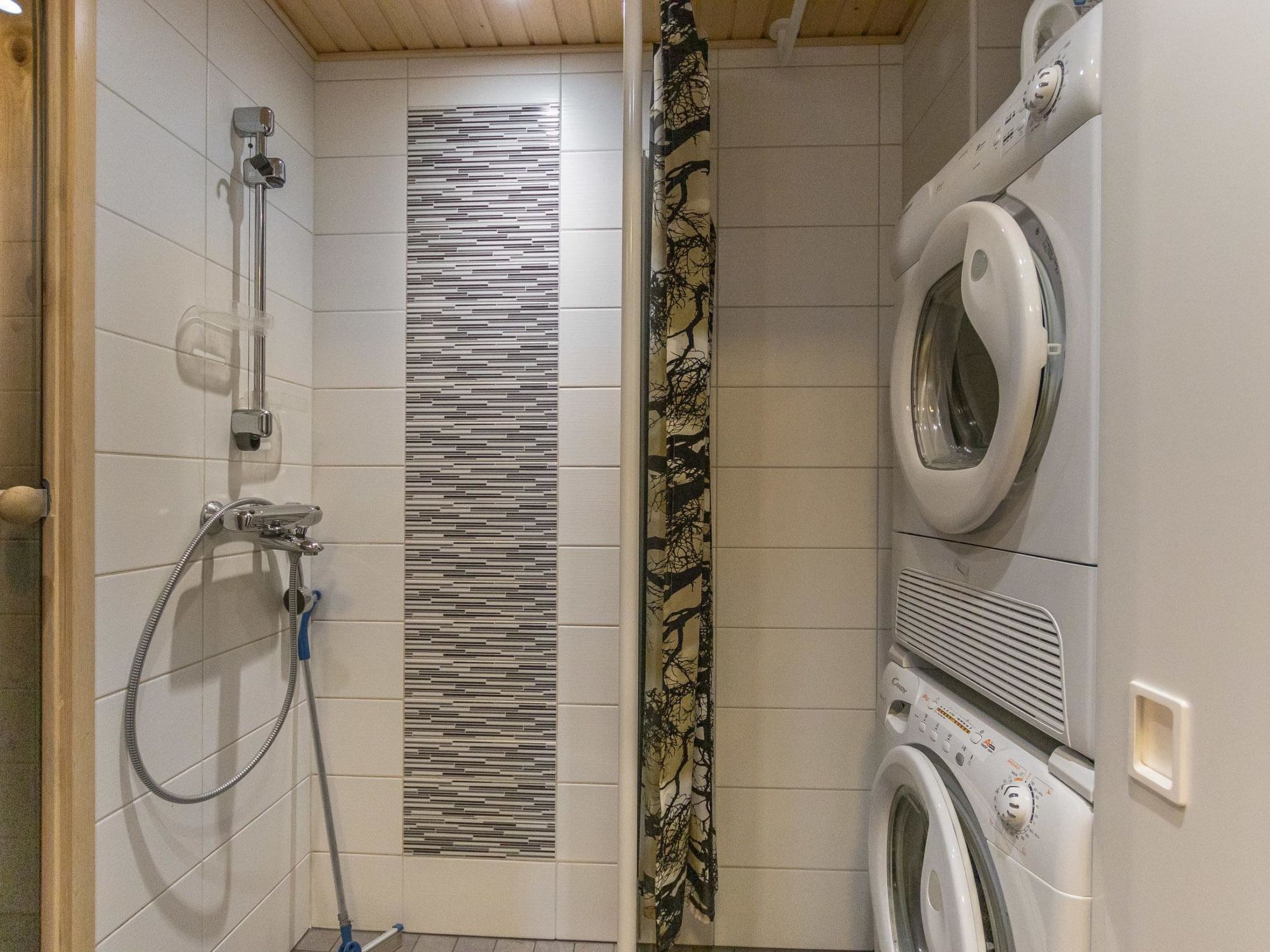 A bathroom with a shower, a patterned wall, a curtain, and a front-loading washing machine.