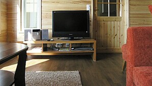 Un intérieur en bois avec un téléviseur posé sur un meuble en bois, une chaise rouge et une porte avec une fenêtre.