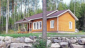 Une cabane en bois dotée d’un porche, entourée d’un mur de pierres et d’arbres.