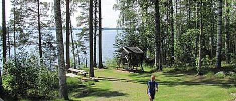 Una cabaña con un balcón que da a un lago, rodeada de árboles altos.