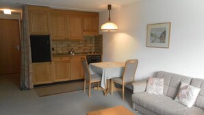 A compact living space with a kitchenette, a dining table with two chairs, a sofa, and a small wooden table. - Ammerten A17 by Interhome (Lenk)