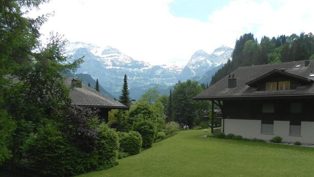 A house with a sloped roof, surrounded by lush greenery and mountains in the background. - Ammerten A17 by Interhome (Lenk)