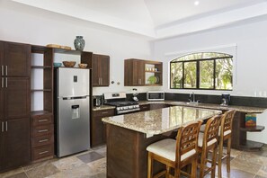 Eine moderne Küche mit dunklen Holfschränken, einem Edelstahl-Kühlschrank, einem eingebauten Backofen und einer Kochinsel mit Granitplatte und Barhocker.