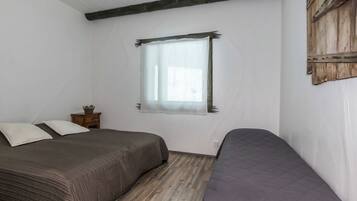 Ein Schlafzimmer mit zwei Betten, einem Fenster mit Vorhang, Holzboden und einem Holzkopfende.