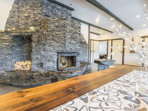 A stone fireplace with a wooden mantel, a fire pit, and a decorative vase with white flowers. - Kivipirtti by Interhome (Keuruu)