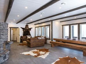 A spacious living room with a stone wall, leather sofas, a large wooden table, and a stone fireplace.