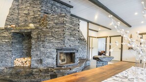 A stone fireplace with a wooden mantel, a stack of firewood, and a decorative vase with white berries. - Kivipirtti by Interhome (Keuruu)
