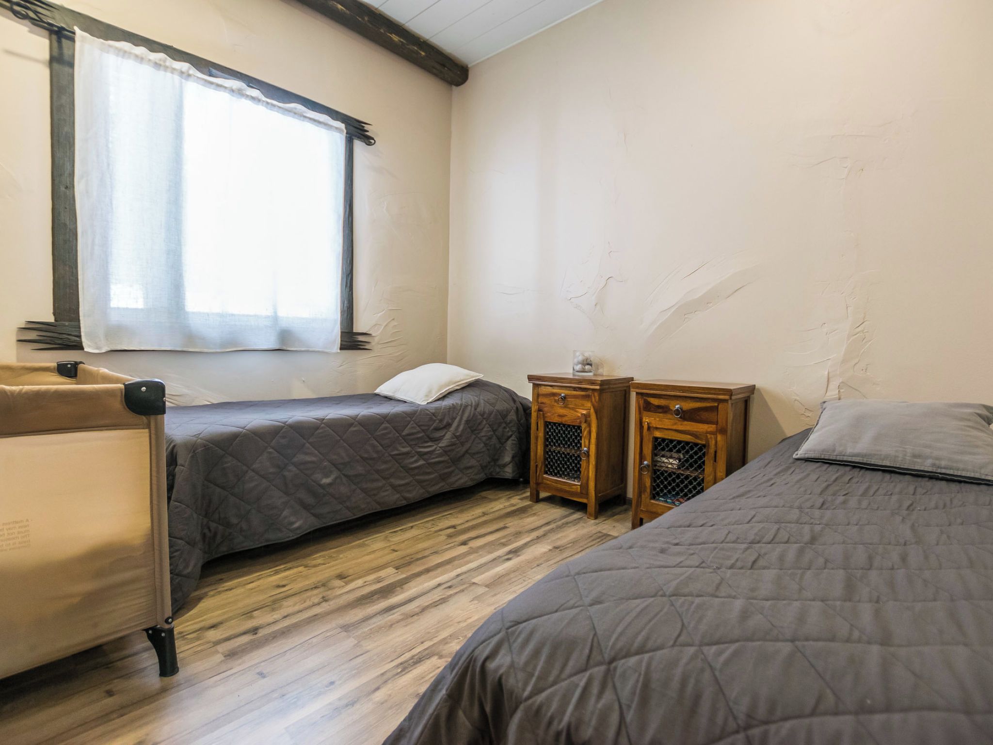 A room with two beds, a window with curtains, and a small wooden table.