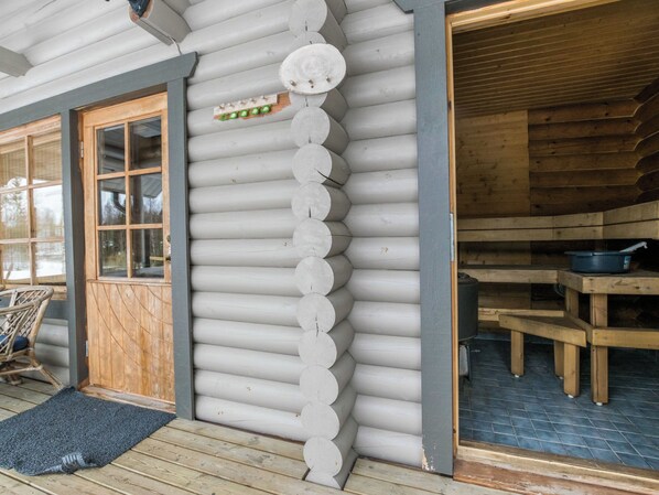 A log cabin with a wooden door, a set of stairs leading to a deck, and a dining area with a table and chairs.