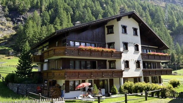 Un chalet à deux étages doté de balcons, niché au cœur d’un paysage montagneux.