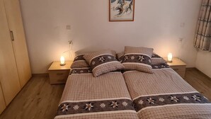 Une chambre à coucher comprenant un lit, deux tables de chevet, une commode, un tableau accroché au mur et une fenêtre avec des rideaux.