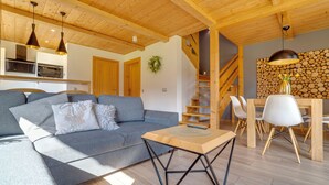 Una sala moderna con un sofá gris, mesa de comedor de madera y una escalera que lleva a un nivel superior.