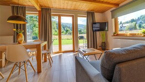 Una habitación acogedora con techo de madera, una zona de comedor con mesa y sillas, un sofá, un televisor montado en la pared y una ventana con vistas a zonas verdes.