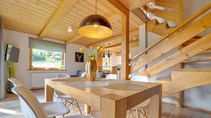 Un interior moderno con una mesa de comedor de madera, sillas blancas, una lámpara colgante grande y una escalera.