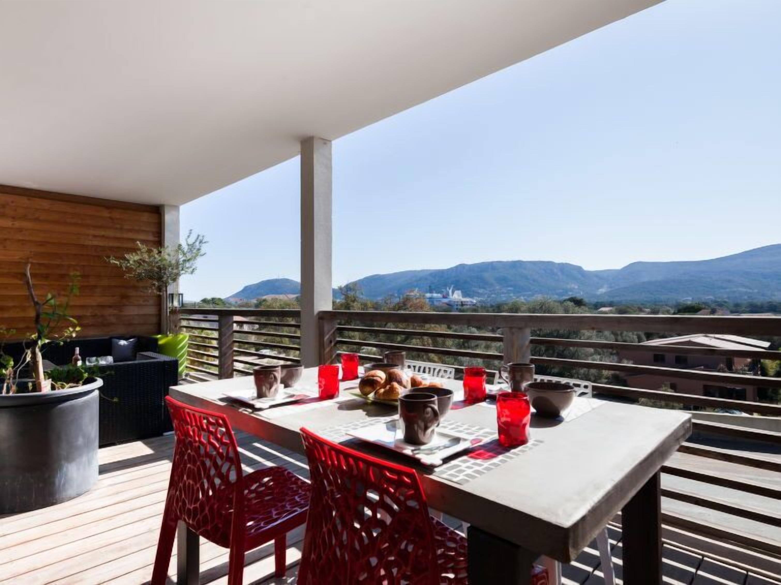 Une terrasse en bois avec une table et des chaises rouges, offrant une vue sur un paysage montagneux.