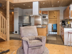 A modern kitchen with a central island, a built-in microwave, and a seating area with a cushioned chair. - Syvärinkulta b by Interhome (Nilsiä)