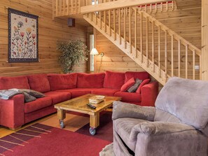 A cozy living room with a wooden staircase, a red sofa, a grey armchair, and a coffee table. - Syvärinkulta b by Interhome (Nilsiä)