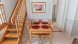Een eetruimte met een houten tafel en stoelen, een trap en een deur die naar een andere kamer leidt.