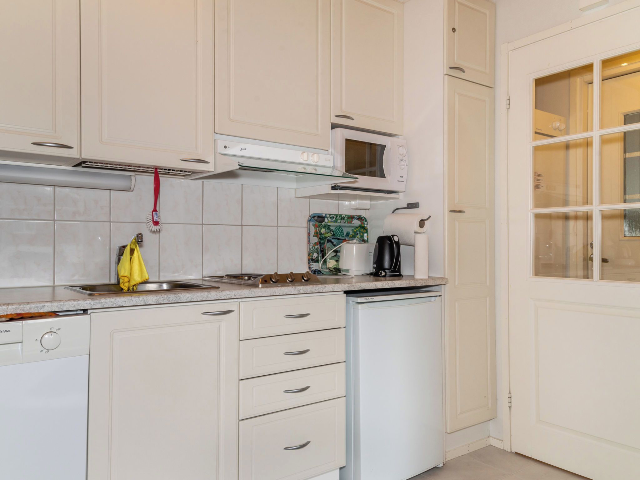 Una cocina con armarios blancos, microondas, hervidor y cafetera.
