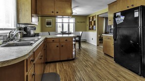 A kitchen with wooden cabinets, a black refrigerator, and a window with blinds.