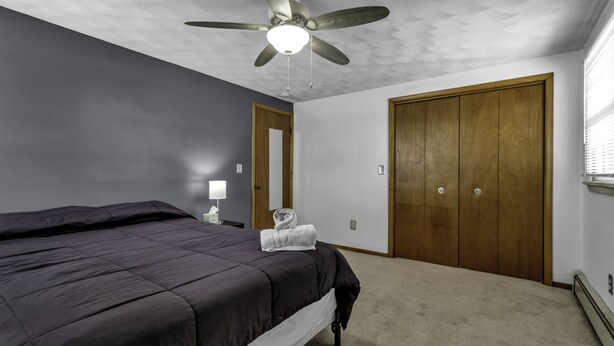 A bedroom with a bed, a ceiling fan, a nightstand, a lamp, and a closet.