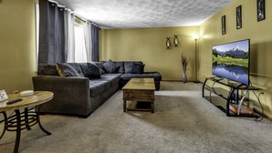 A living room with a sofa, coffee table, TV stand, and a lamp.