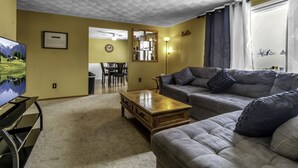 A living room with a sofa, a coffee table, a TV, and a dining area with chairs and a table.