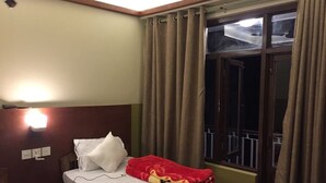 Quarto de hotel com cama, luz noturna, janela com cortinas e vista para o exterior.