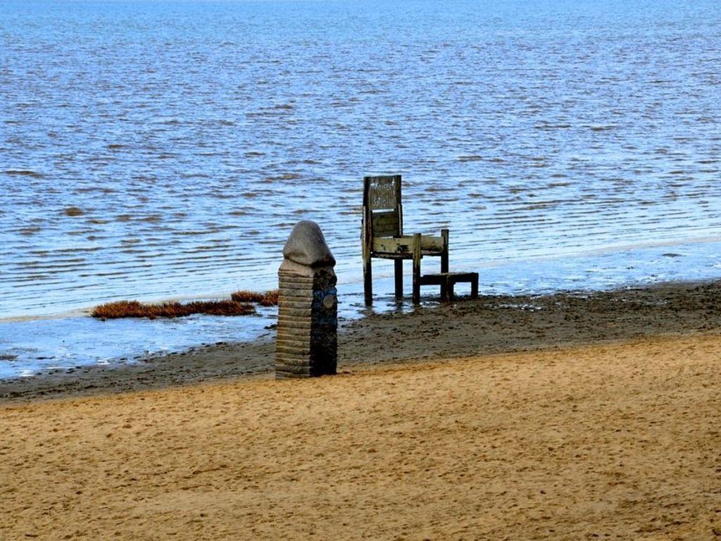 Ein Strand mit einer Steinstruktur und einem Holzstuhl am Wasser.