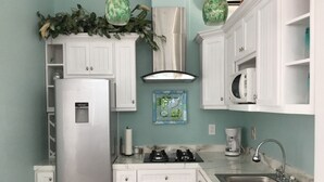 Una cocina con armarios blancos, un refrigerador, un microondas, un lavamanos y una estufa.