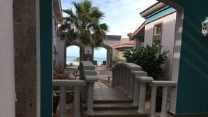 Un pasillo con vista a la playa, una palmera y un piso de baldosas con diseño geométrico.