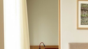 Un dormitorio con una cama de madera, una mesita de noche, un almohadón rojo y una lámpara fijada a la pared.