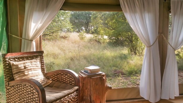 Une chaise en osier avec un coussin et une petite table en bois sur laquelle repose un livre.