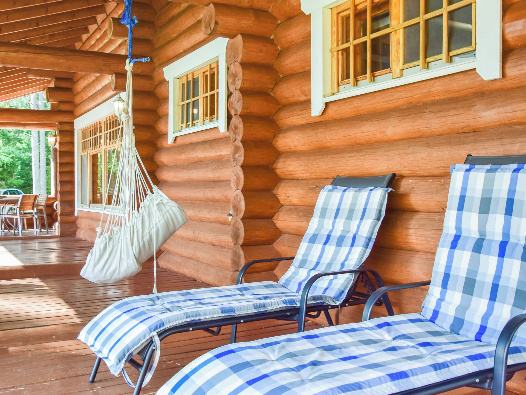 A log cabin with two lounge chairs and a hammock.