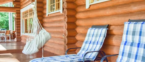 A log cabin with two lounge chairs and a hammock.