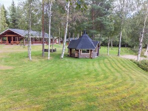 A log cabin with a conical roof surrounded by a well-maintained lawn and birch trees.