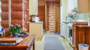 L’intérieur d’une cabane en rondins comprend une cuisine, des murs en bois et un coin repas avec une table et des chaises.
