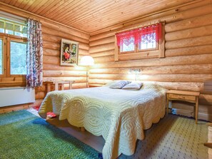A log cabin bedroom with a bed, a nightstand, a lamp, and a window with curtains.
