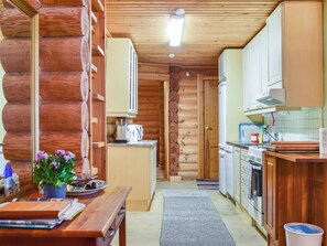 A log cabin interior with a kitchen area, wooden walls, and a dining table with a plant. - Kivitasku by Interhome (Ikaalinen)