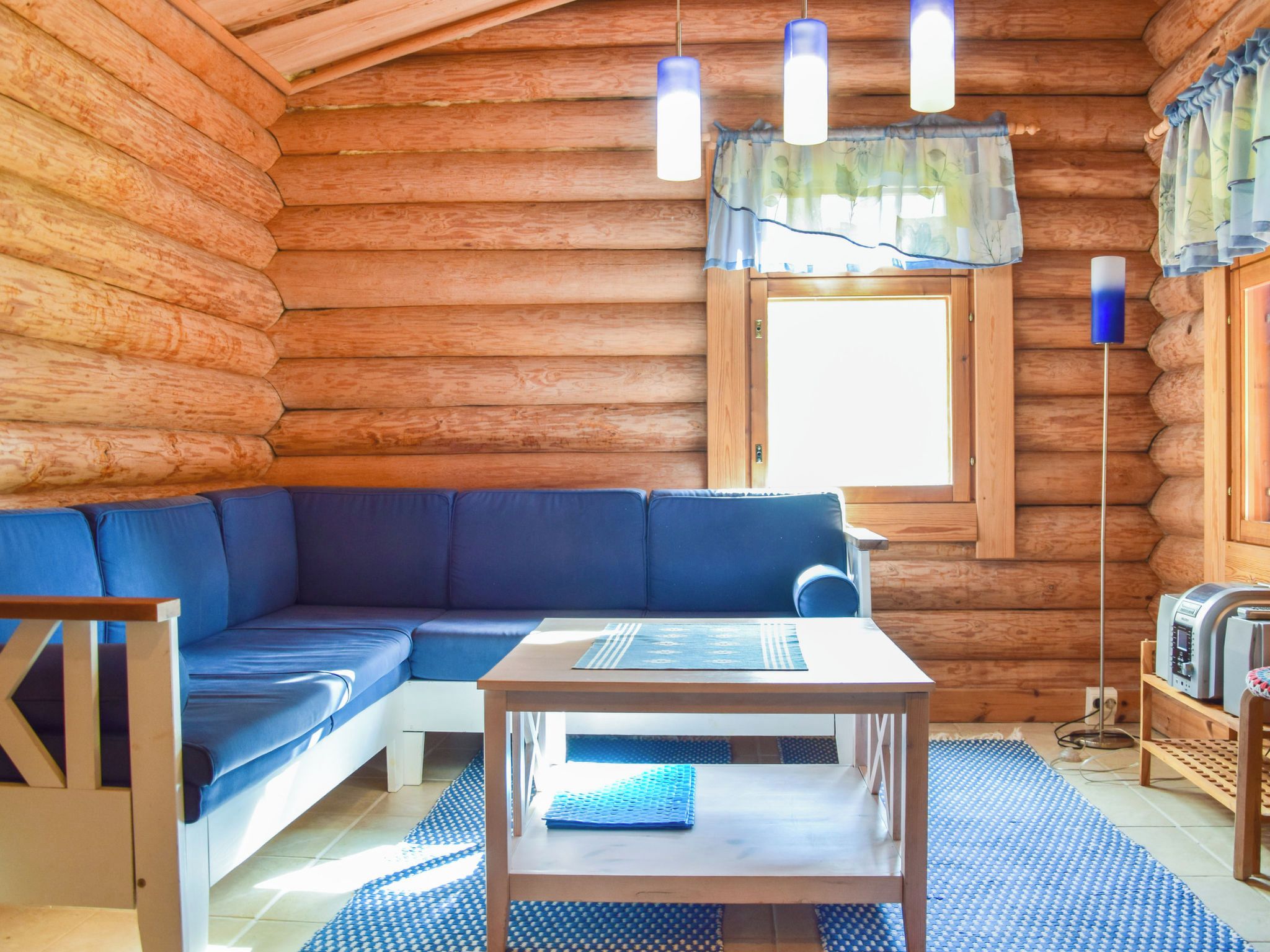 A log cabin interior with a blue sofa, a small table, and a window with curtains.