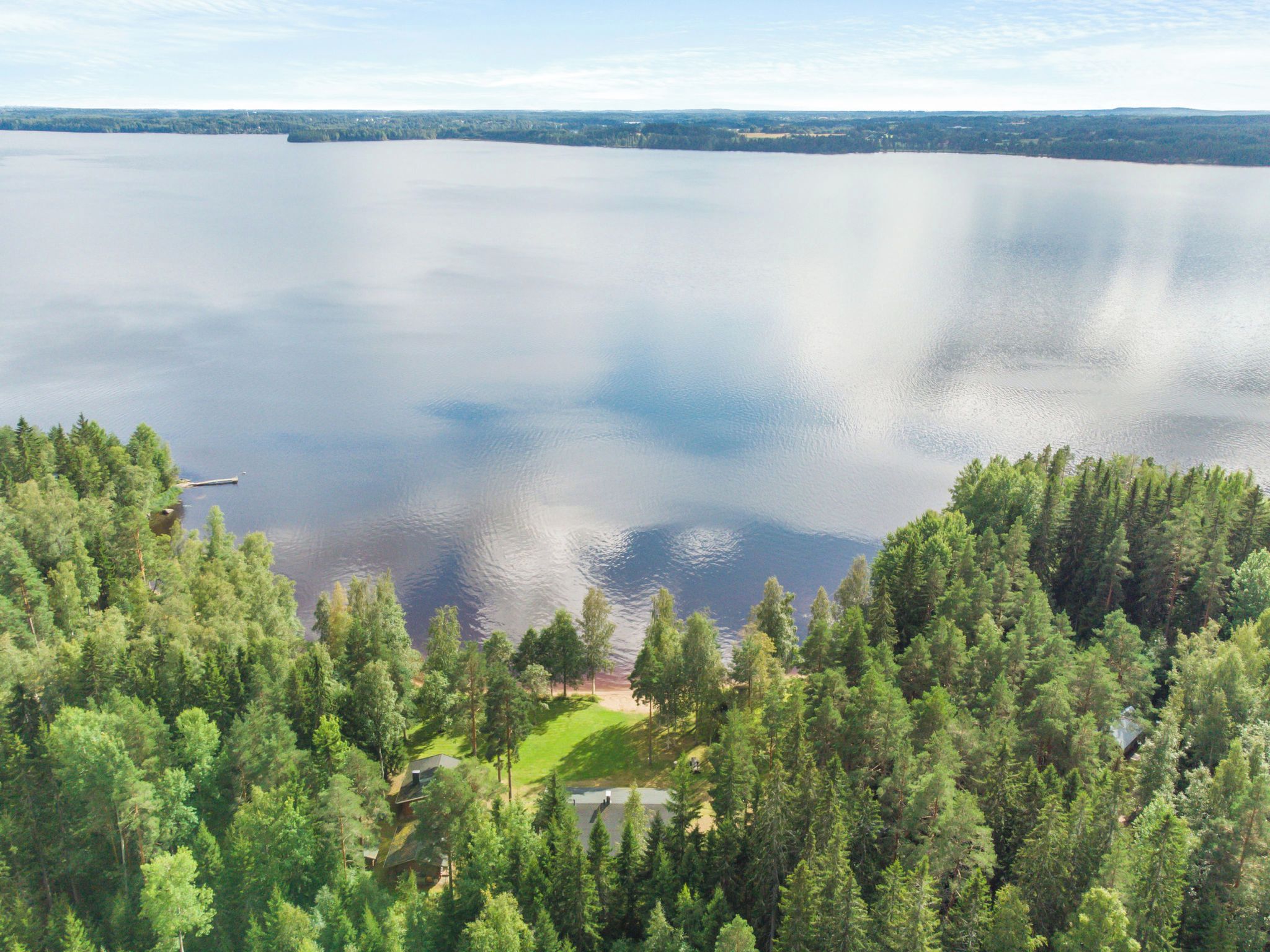 A lake surrounded by dense forest with a small clearing and a dock.